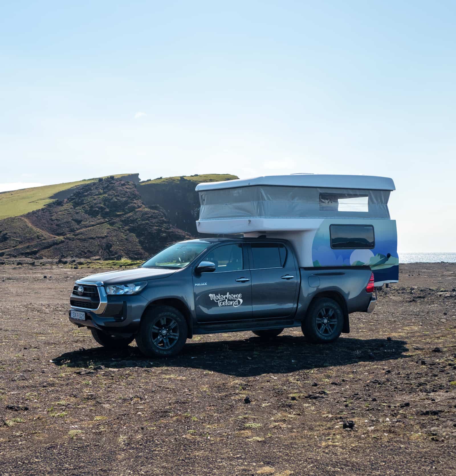  Camper Toyota Hilux bajo el sol, aparcada en una F-Road de grava sin asfaltar.